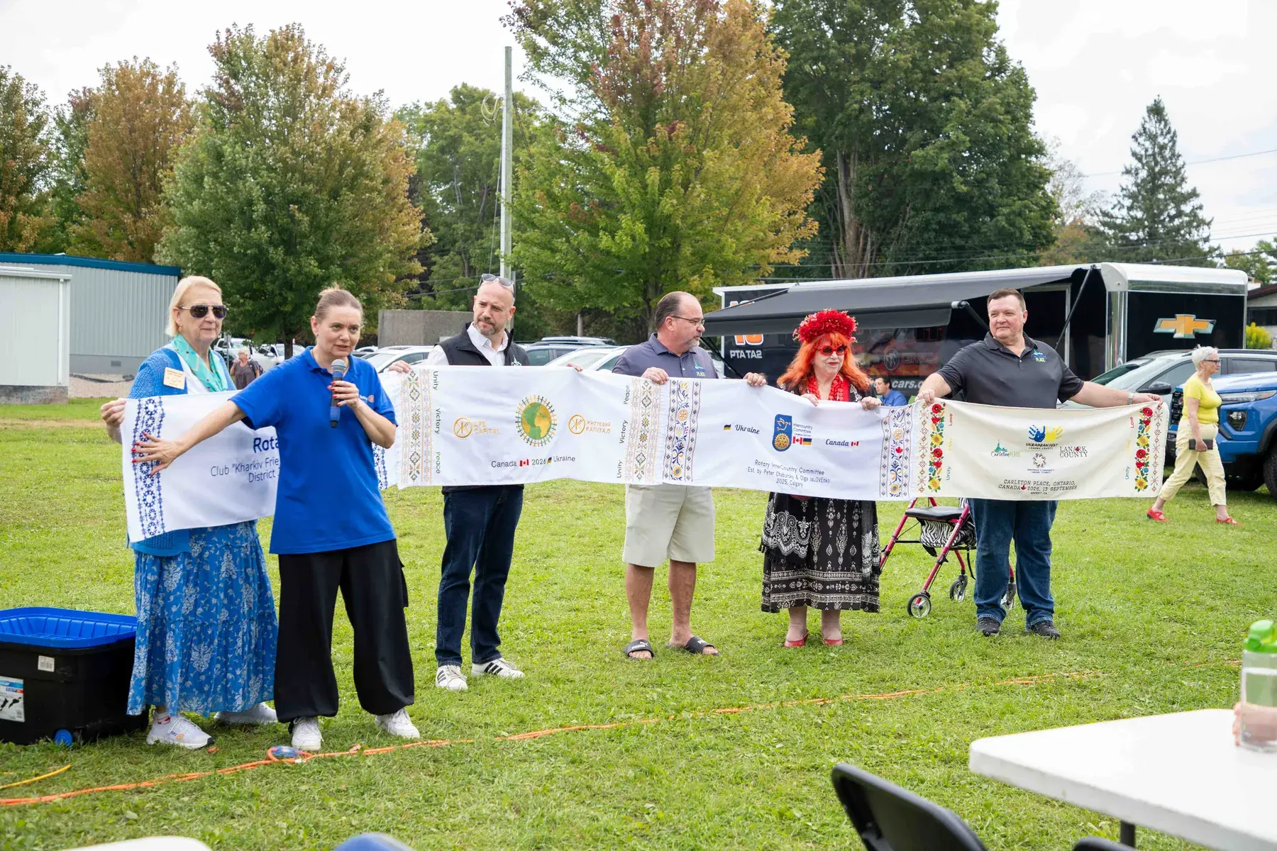 Guests and organizers hold the unrolled rushnyk on the grass of Riverside Park