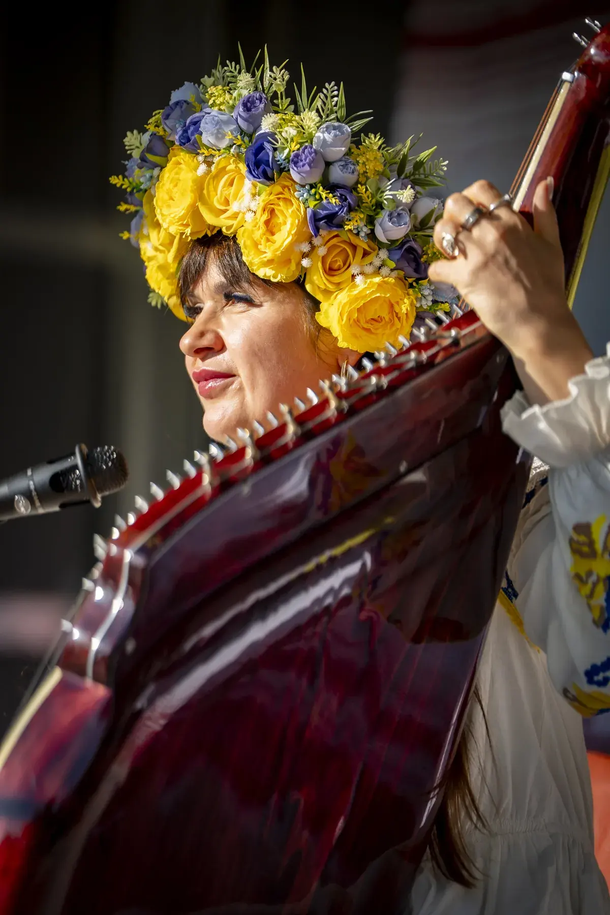 Bandura player in a flower crown singing, close-up behind the instrument