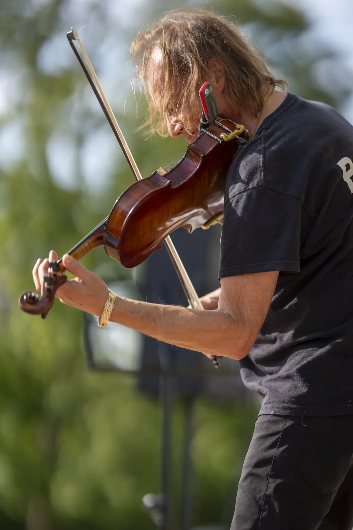 Vasyl Popadiuk at UAFest 2026 — Violinist in a black T-shirt plays on stage against green trees (photo: Tim Skinner)