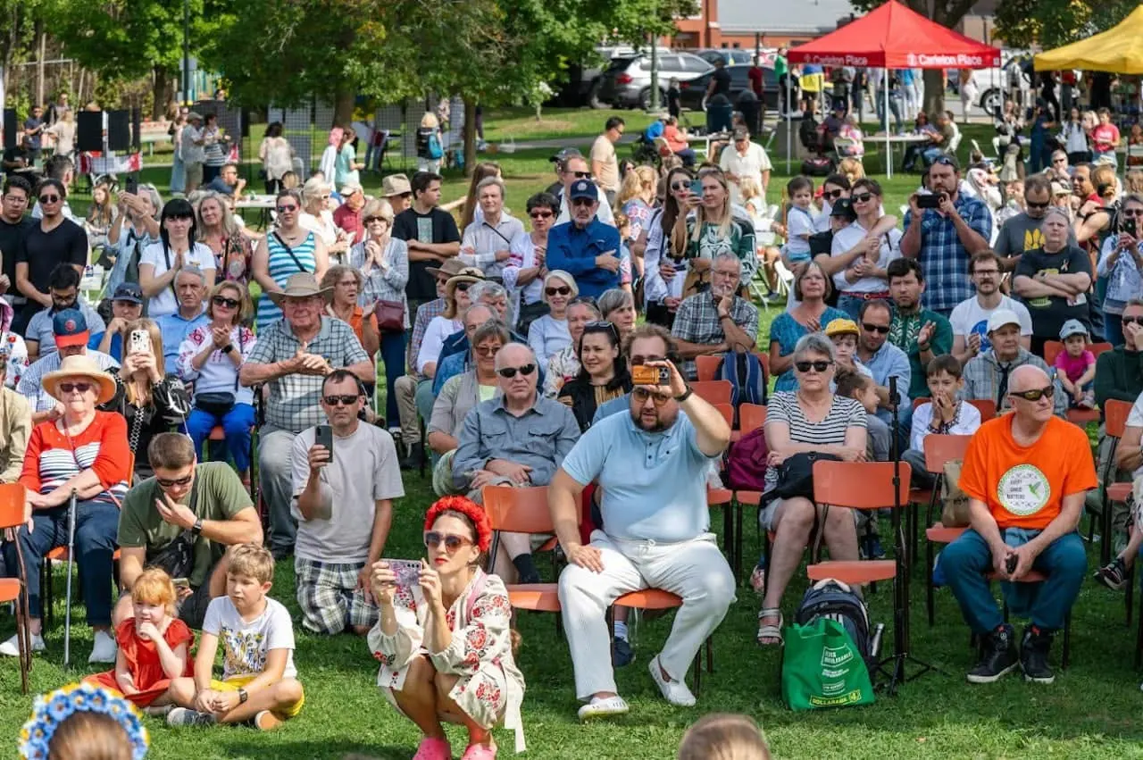 Festival-goers gathered on the lawn at Riverside Park with the trees and open parkland of Carleton Place around them