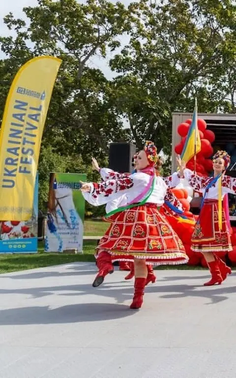 Dancers in red-and-gold embroidered folk costumes performing mid-spin on the outdoor festival stage.