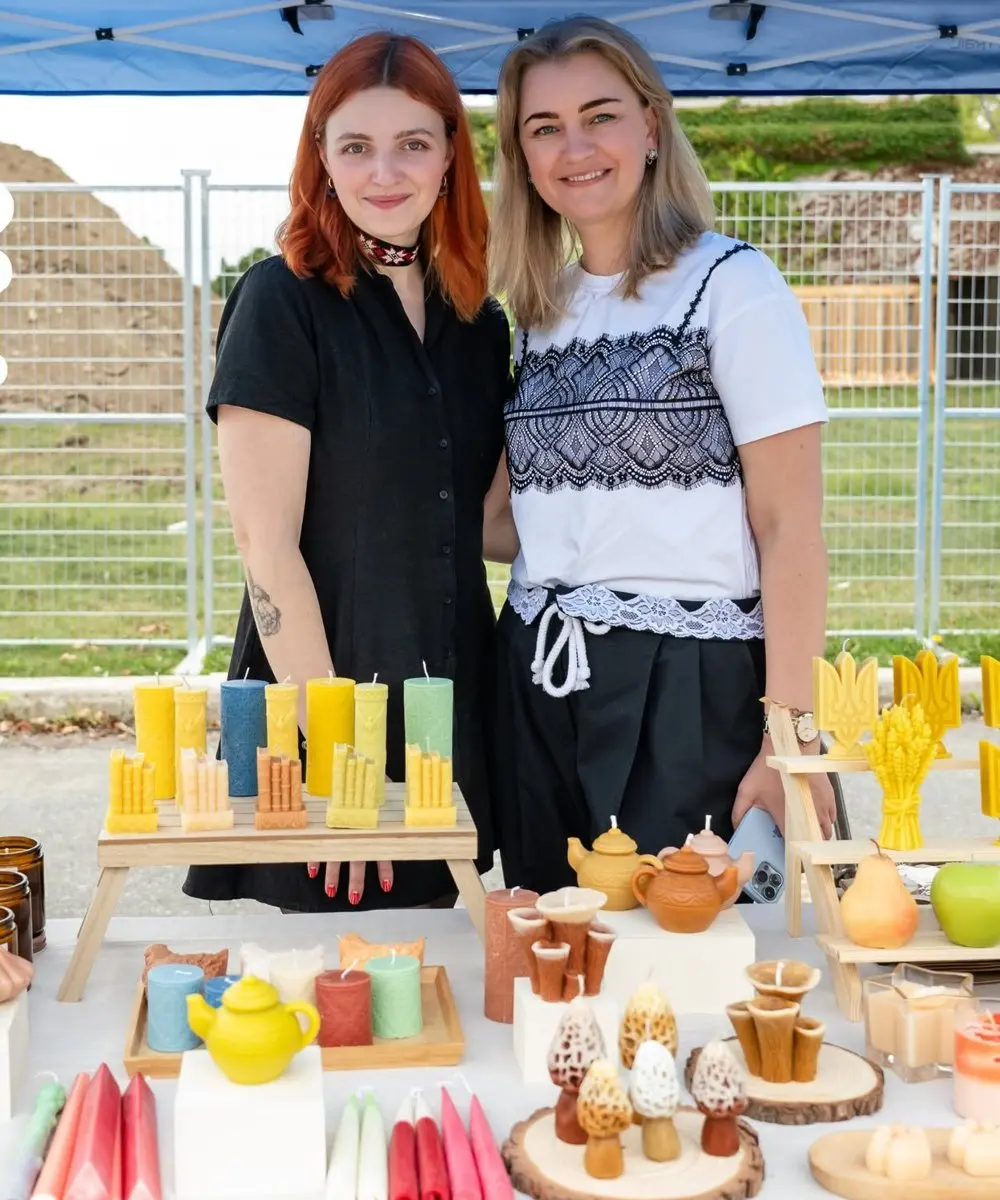 Two vendors smiling behind a market stall of handmade candles at the UAFest food market