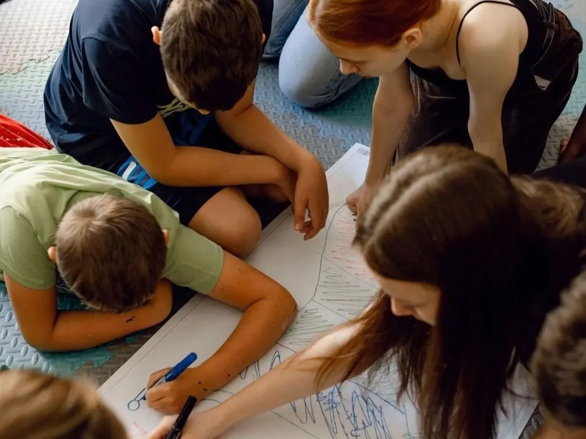 Kids and teens drawing together on a big shared sheet during a hands-on workshop