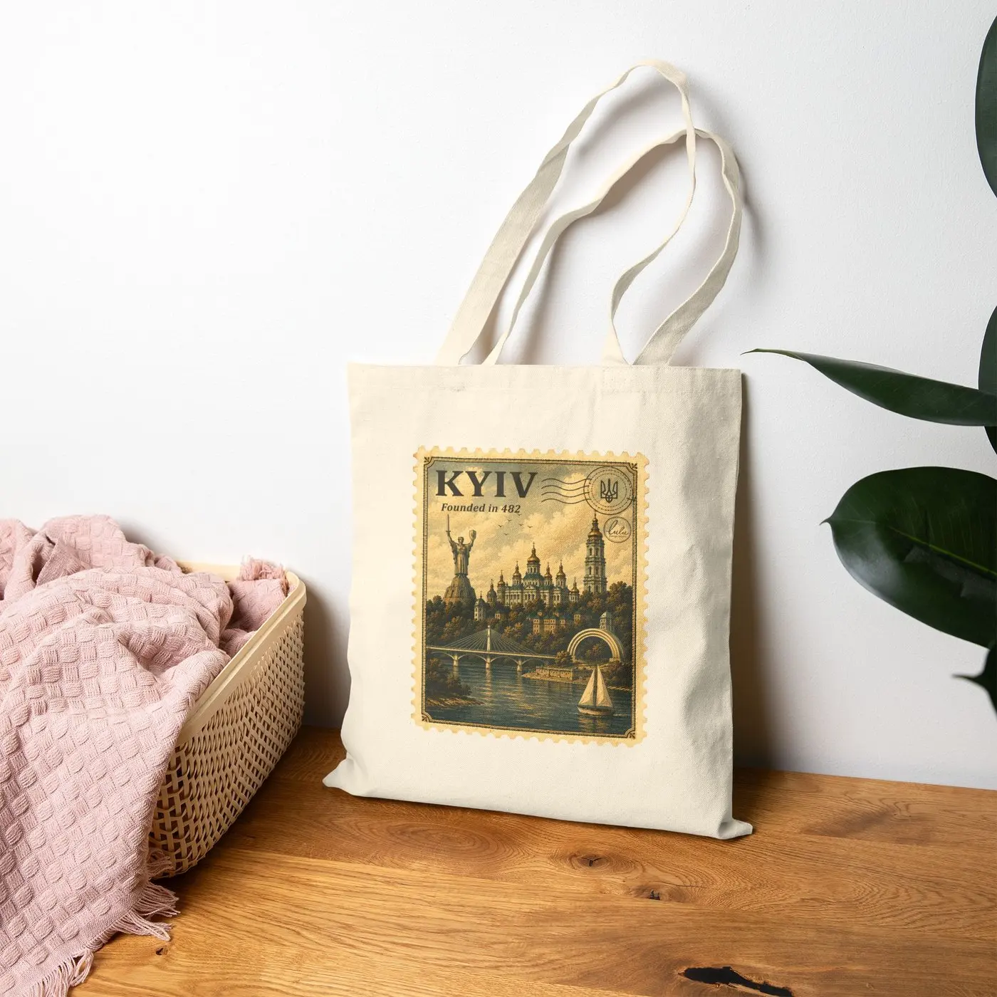 The tote standing on a wooden dresser beside a basket and a houseplant, the Kyiv stamp facing out