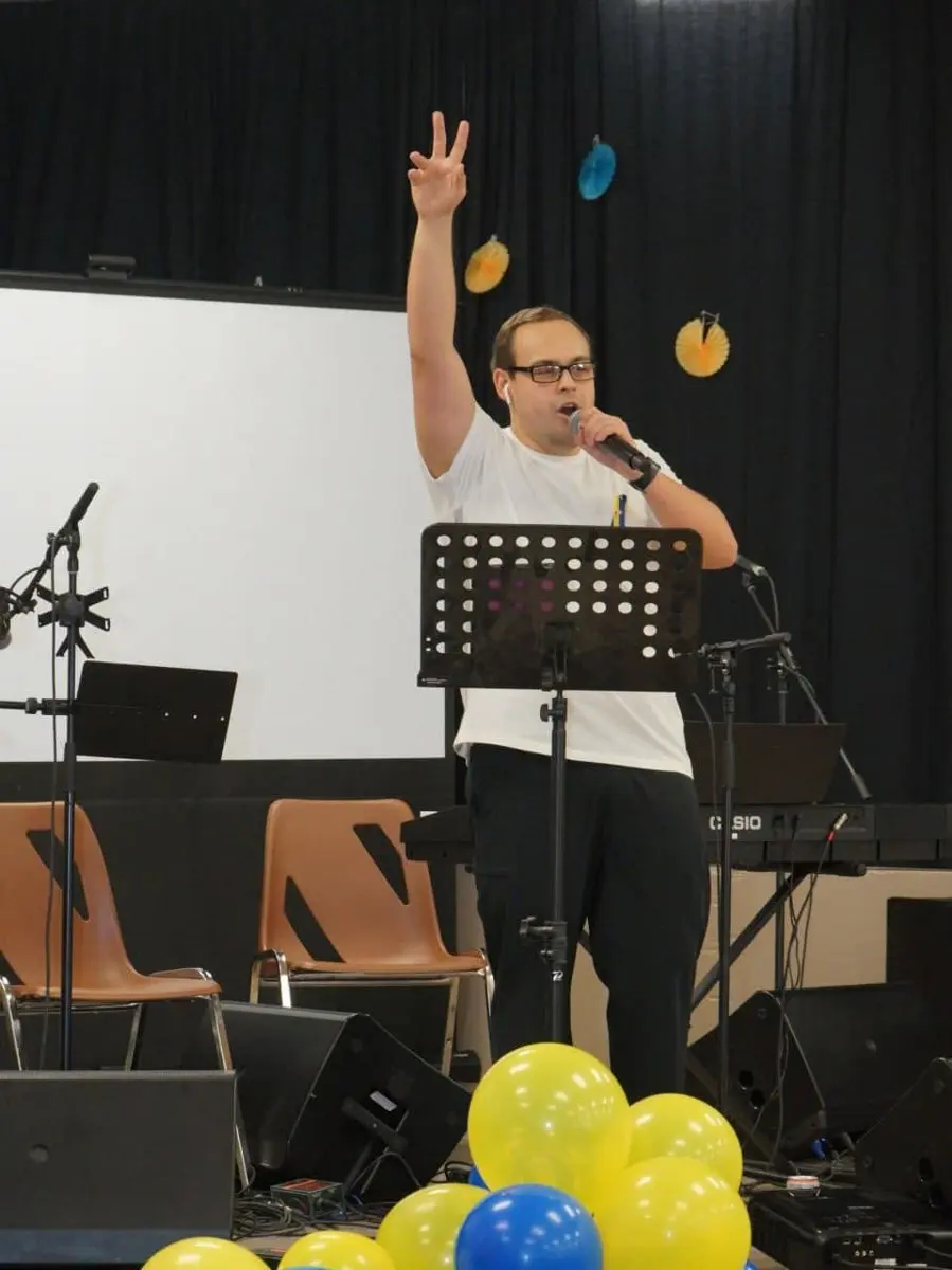 A singer performing on stage with a raised hand, balloon decorations and a keyboard behind him at a past UAFest event.