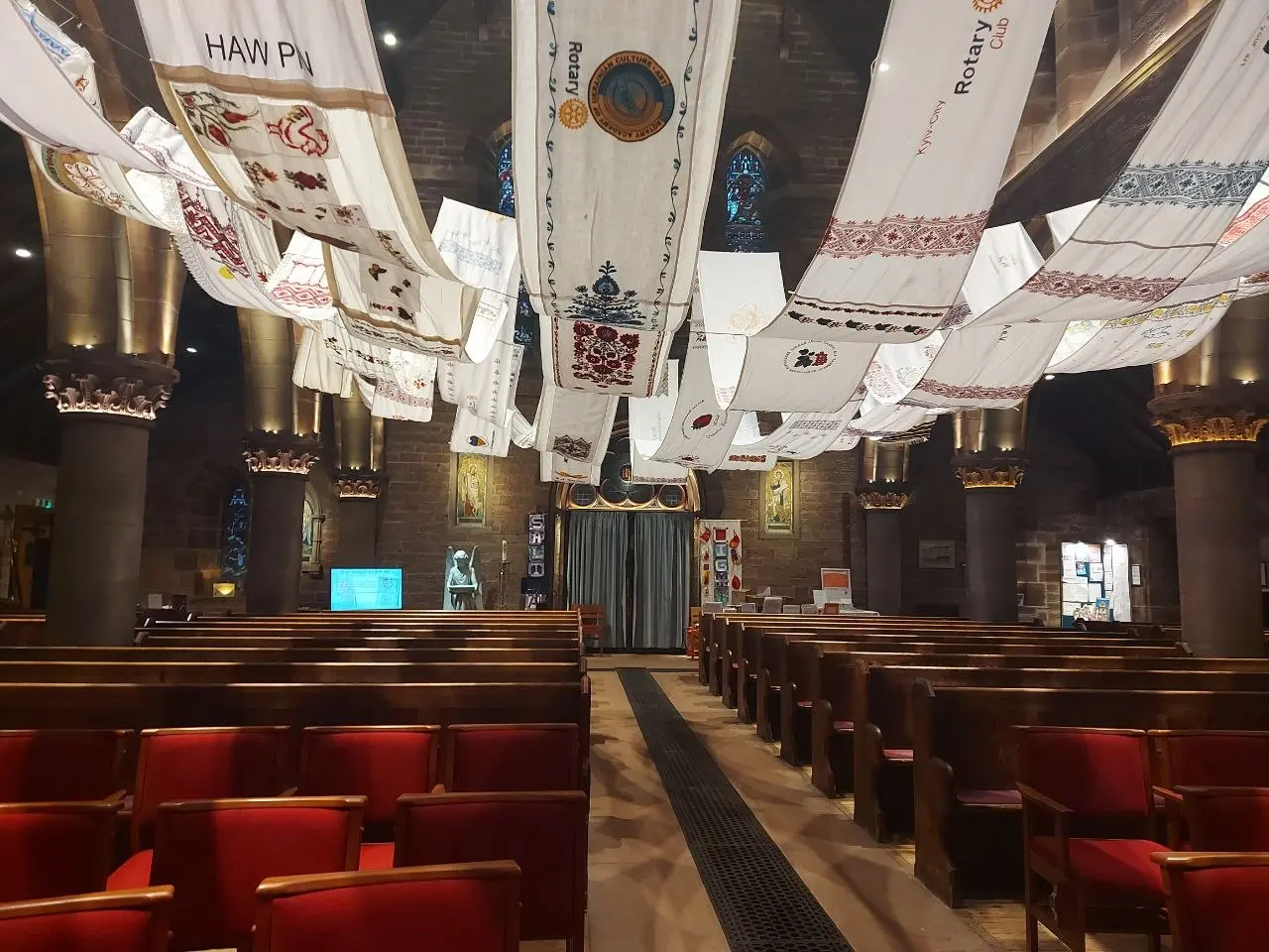 Embroidered rushnyk panels hanging in a church, one with a Rotary emblem