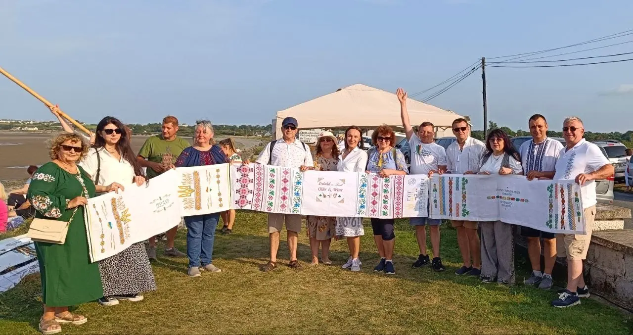 Ukrainian community members in Ireland holding rushnyk panels by the sea