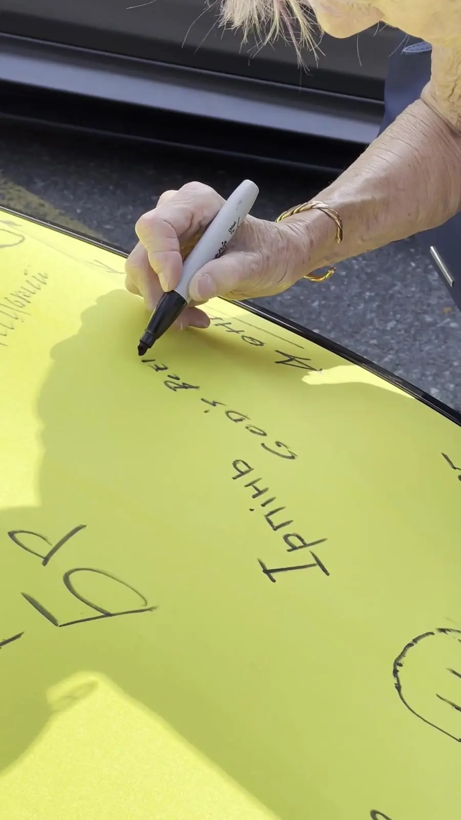 A visitor signing a Ukrainian hometown name on the yellow hood of the flag-painted car at UAFest 2025