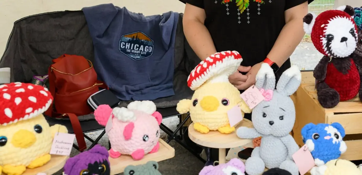 A vendor's tent table set up with handmade crochet toys — mushrooms, chicks, bunnies and a panda — ready for festival visitors