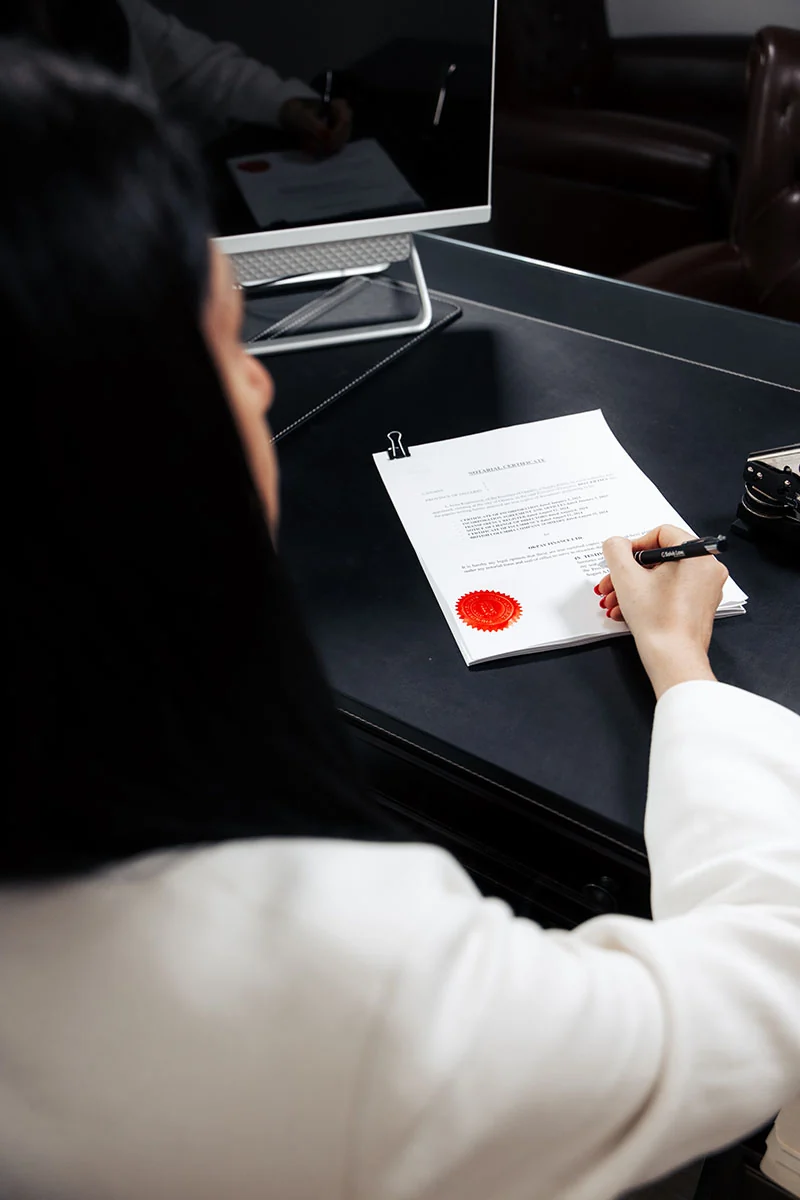 Over-the-shoulder view of a signature being placed on a share certificate with a red corporate seal, on a desk in the Solvis Law office