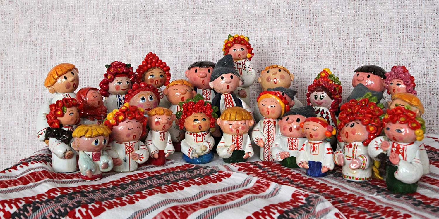A crowd of small painted ceramic figures in Ukrainian dress, arranged singing on a red and black embroidered rushnyk