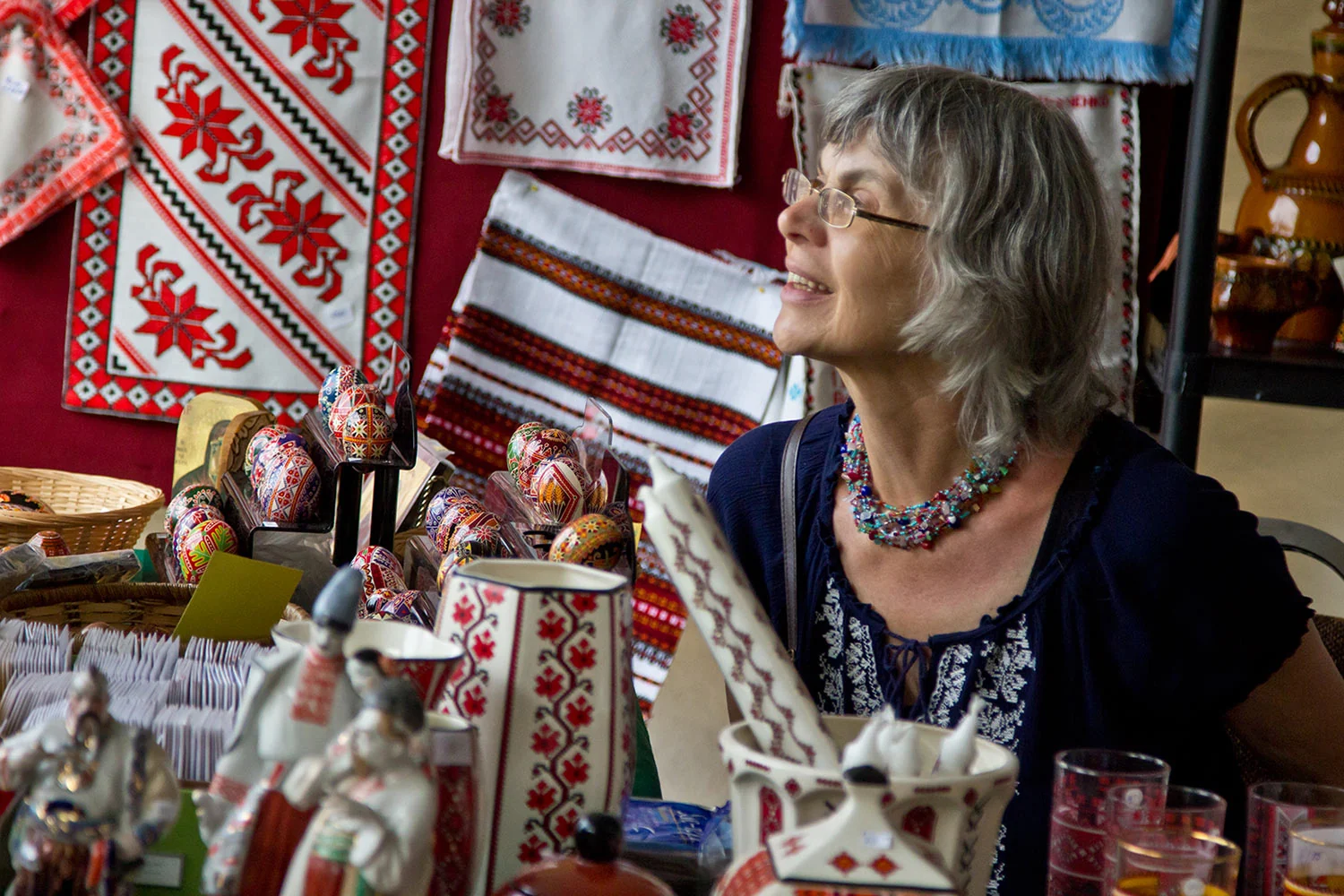 A Yarmarok stall hung with red embroidered cloths, with pysanky, painted ceramics and a jug on the table