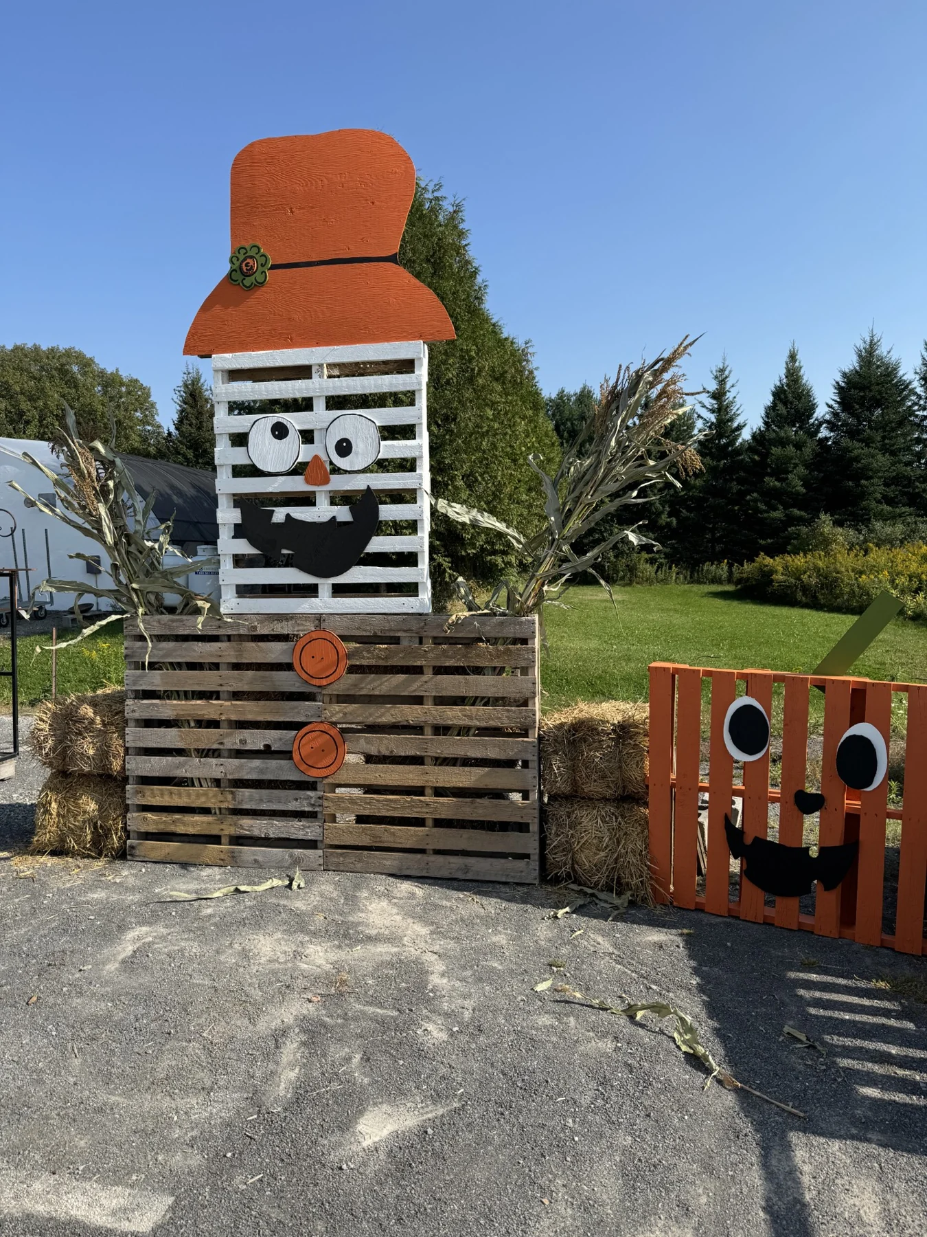 Scarecrow and jack-o'-lantern figures built from painted wooden pallets, straw bales and corn stalks, standing in the nursery yard.