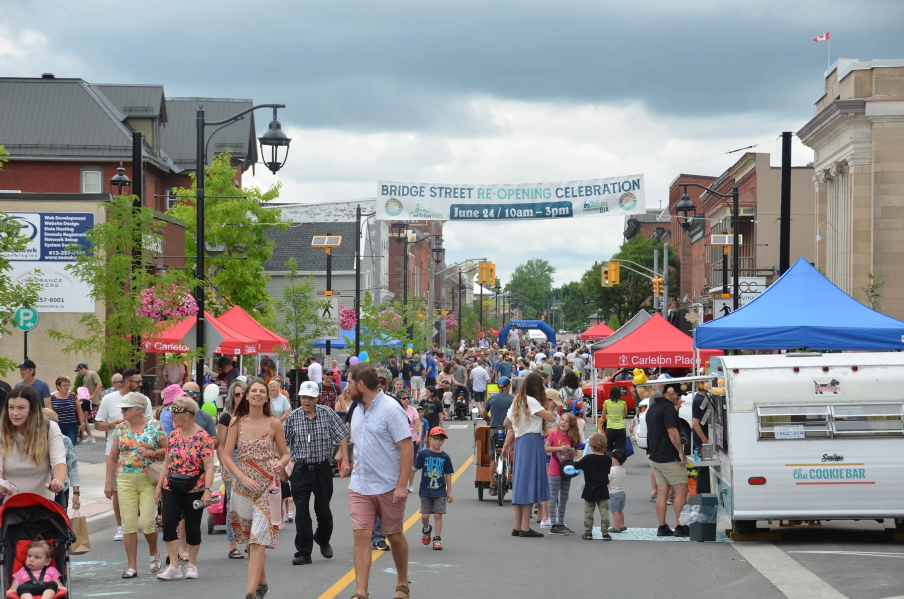 Bridge Street closed to traffic and filled with people, vendor tents and a banner reading Bridge Street Re-Opening Celebration