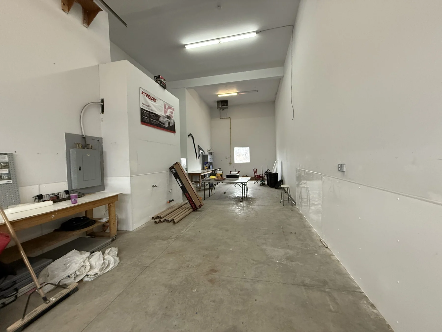 Inside the vacant garage bay at 130 Industrial Avenue: white walls, a concrete floor, a workbench and the electrical panel