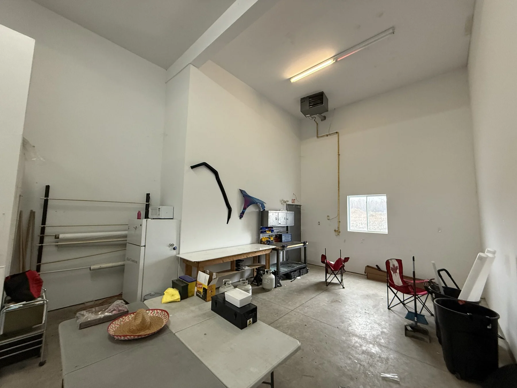 The high-ceilinged rear of the garage bay with a gas unit heater, a small window and folding tables