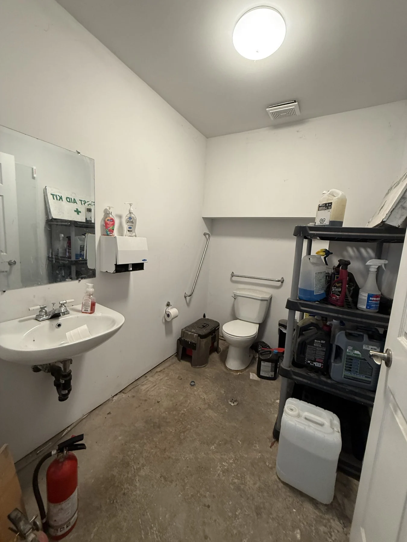 The washroom serving the garage bay, with a wall-hung sink, mirror, grab bars and a fire extinguisher by the door