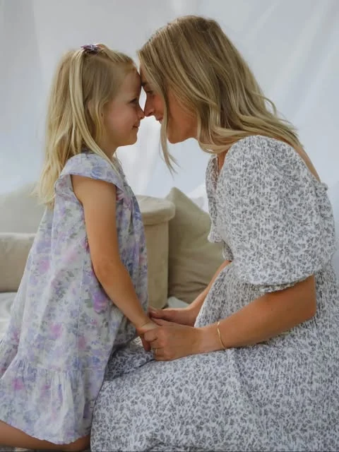 A session of hers — a mother and her daughter forehead to forehead in floral dresses against a pale backdrop