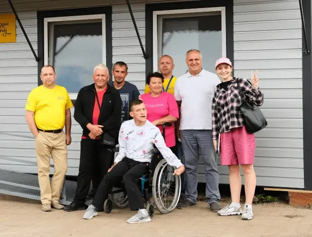 Adults and a young man in a wheelchair posed in front of a newly delivered white modular house
