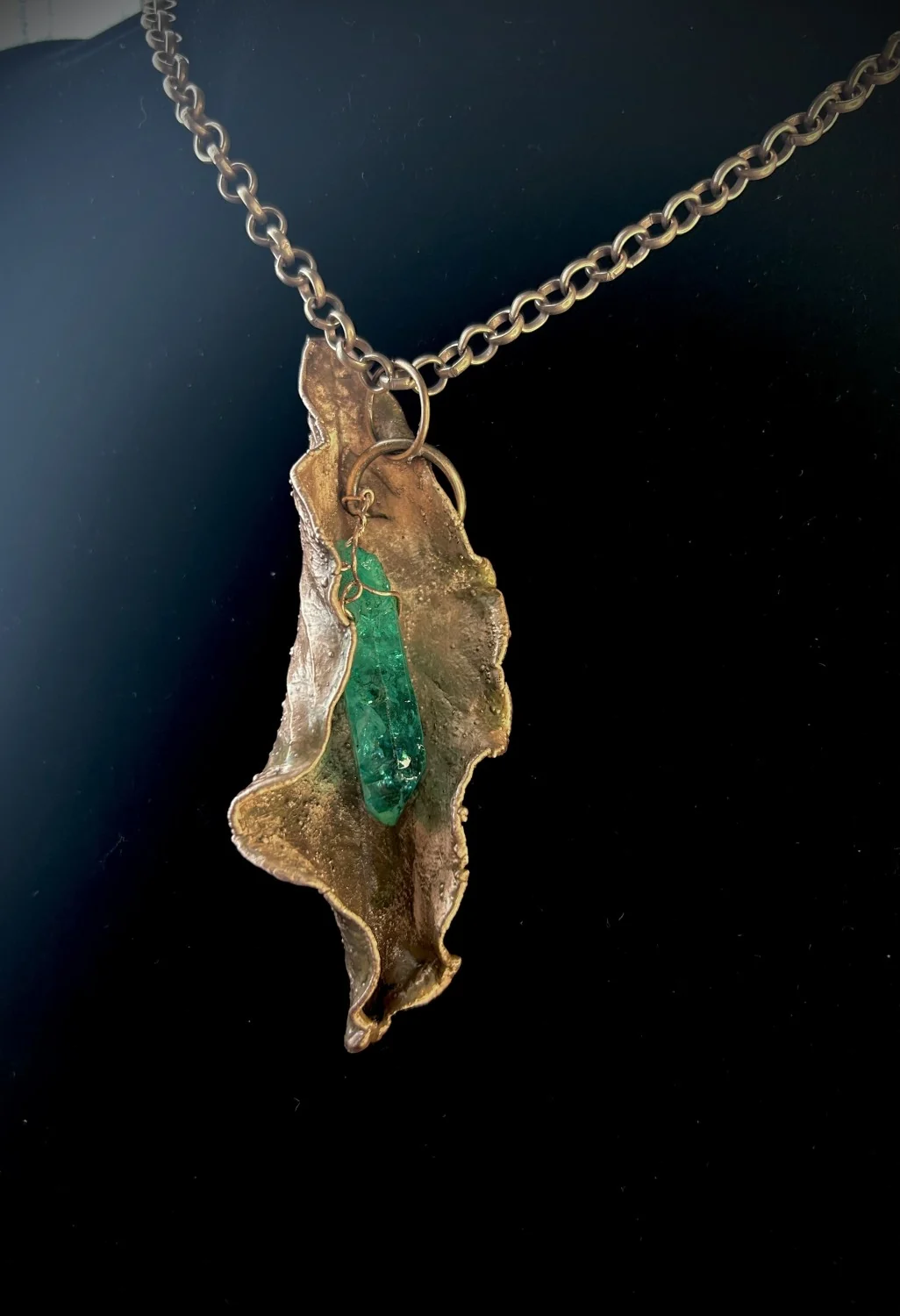 Copper leaf pendant holding a raw green crystal, on a heavy copper chain