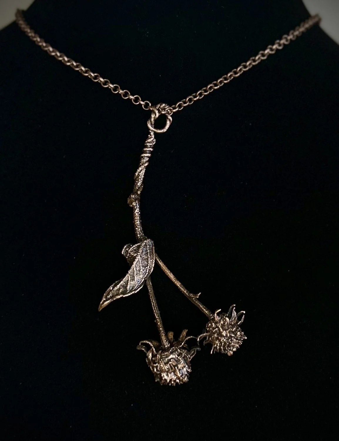 Copper twig necklace with two seed heads and a single leaf, displayed on a black bust