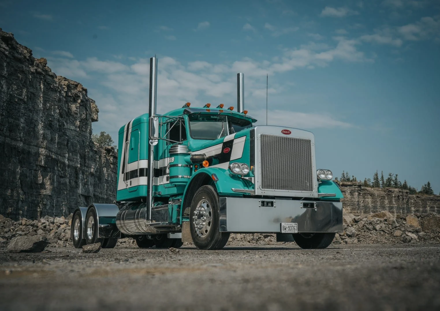 A turquoise Peterbilt highway tractor in Cavanagh colours parked against a grey quarry rock face