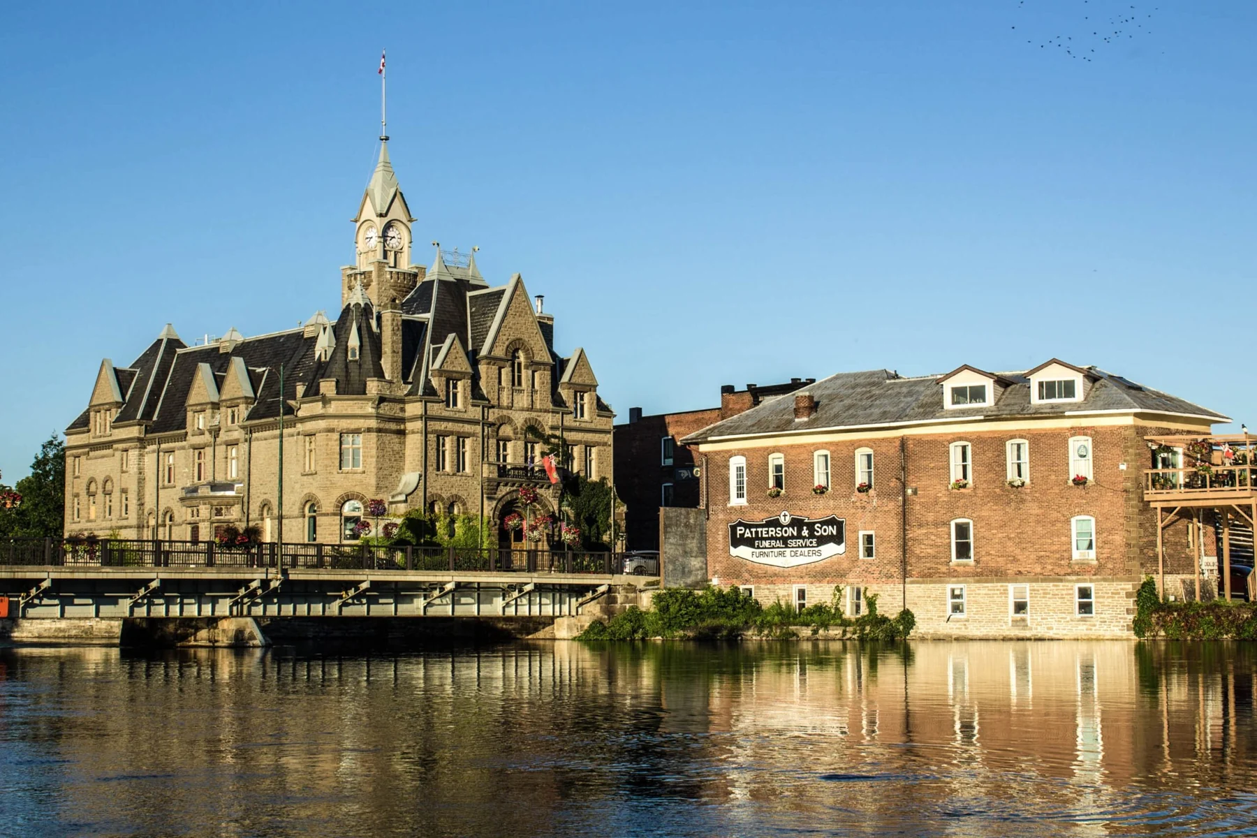 Carleton Place Town Hall — the 1897 stone building with its clock tower — seen across the Mississippi River beside a red-brick neighbour