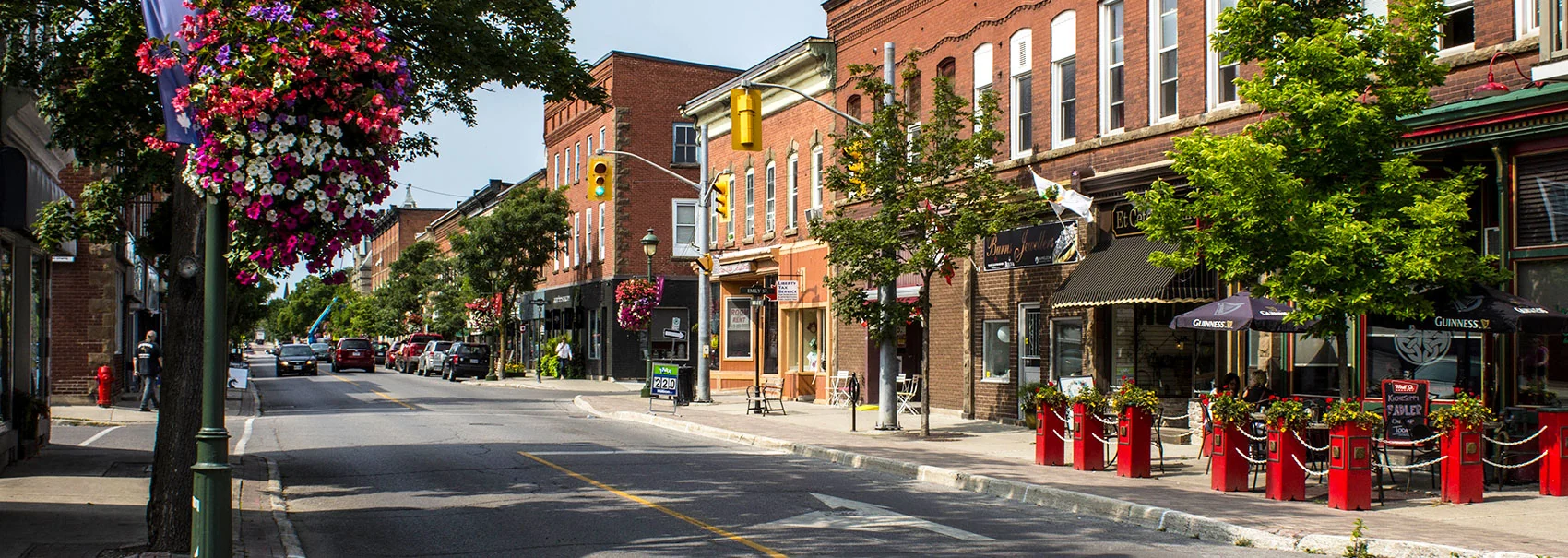 Historic downtown Carleton Place in summer: brick heritage storefronts, hanging flower baskets on the lampposts and patio seating outside the shops