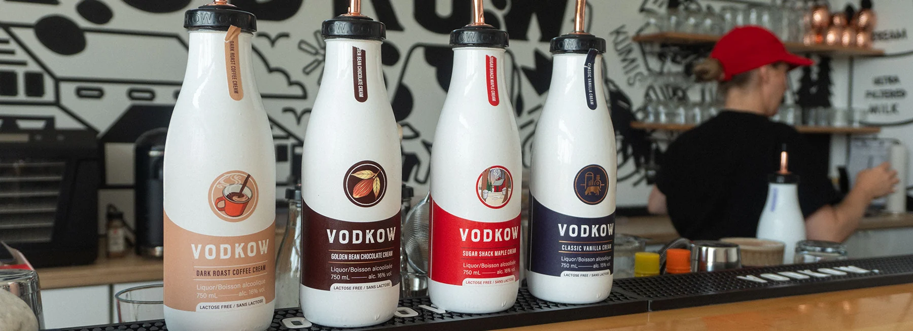 Four Vodkow cream liquor bottles with copper pour spouts lined up on the distillery bar — Dark Roast Coffee, Golden Bean Chocolate, Sugar Shack Maple and Classic Vanilla